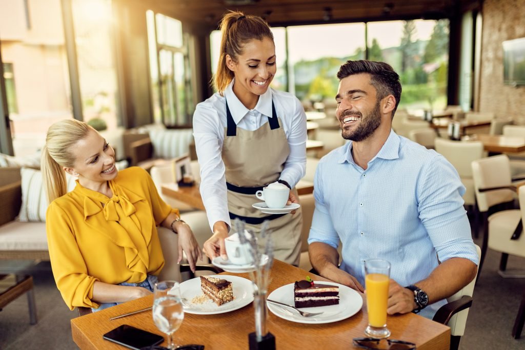Happy couple enjoying in a dessert while the waitress is serving them coffee in a cafe.