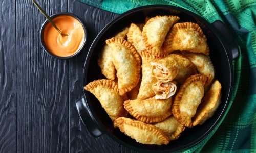 hot juicy Buffalo Chicken Empanadas with Low-Calorie Dip on in a black ceramic pan on a wooden table, horizontal view from above, flat lay, free space